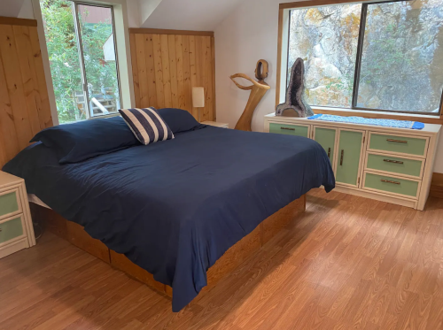 Cozy bedroom with a large bed, wooden walls, and a window showcasing natural scenery outside.